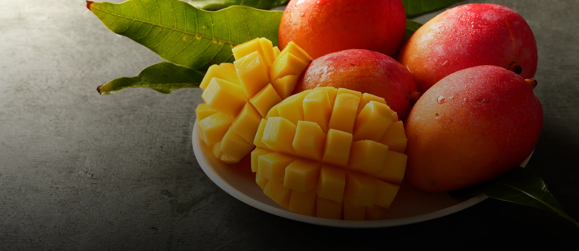 Ripe mangoes and cut pieces on dish